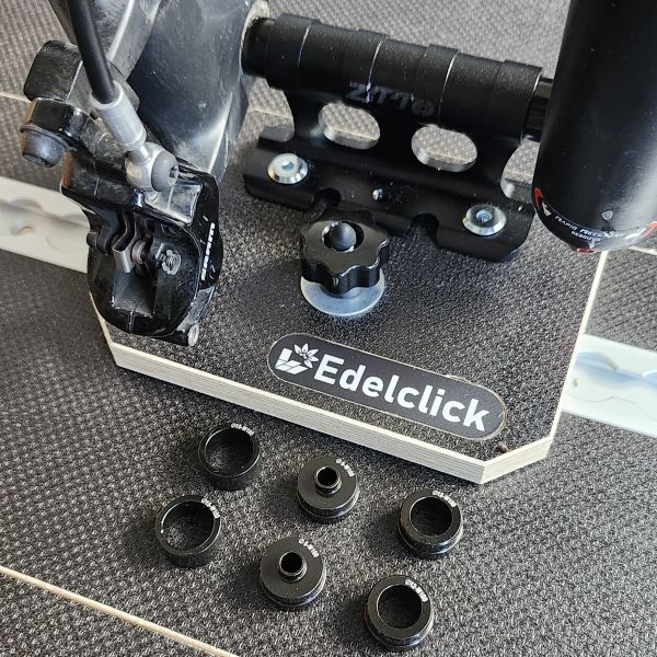 Présentation de notre produit "support axe vélo", fixé sur un rail aéro. Un vélo est monté sur ce support par sa fourche avant et différentes calles d'adaptation selon le type de fourche sont disposées à proximité.